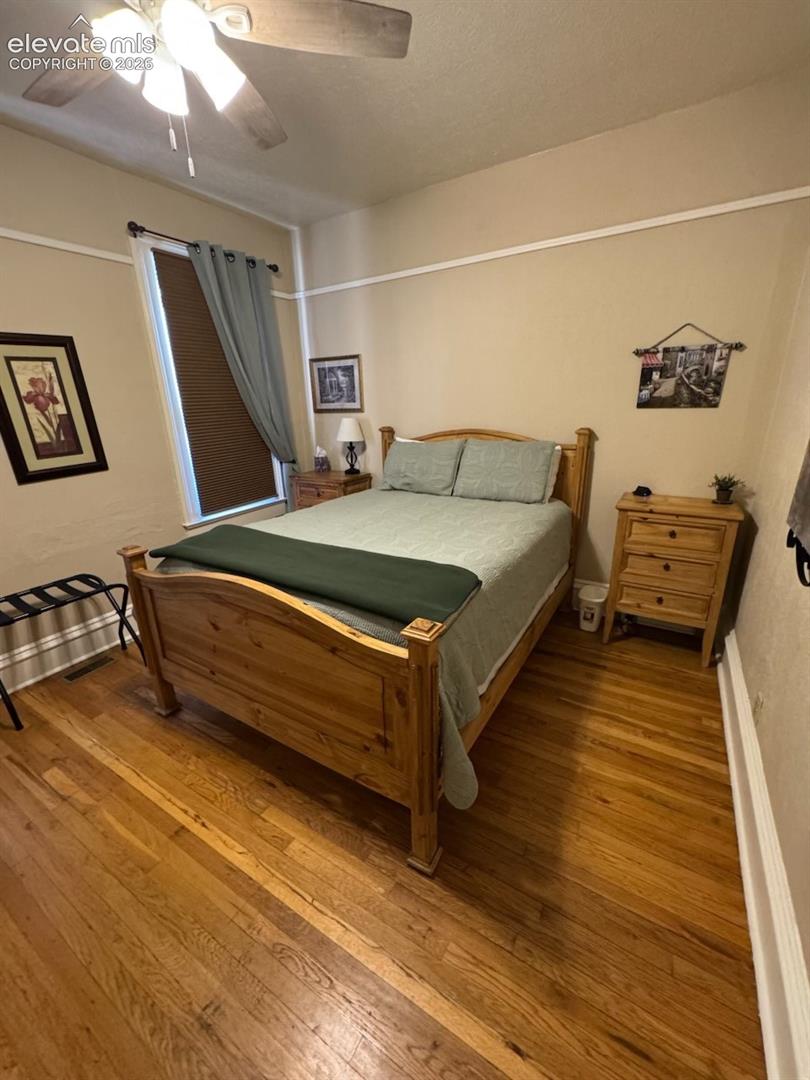 Wood-finish flooring, ceiling fan with integrated lighting, window with blinds, and decorative trim