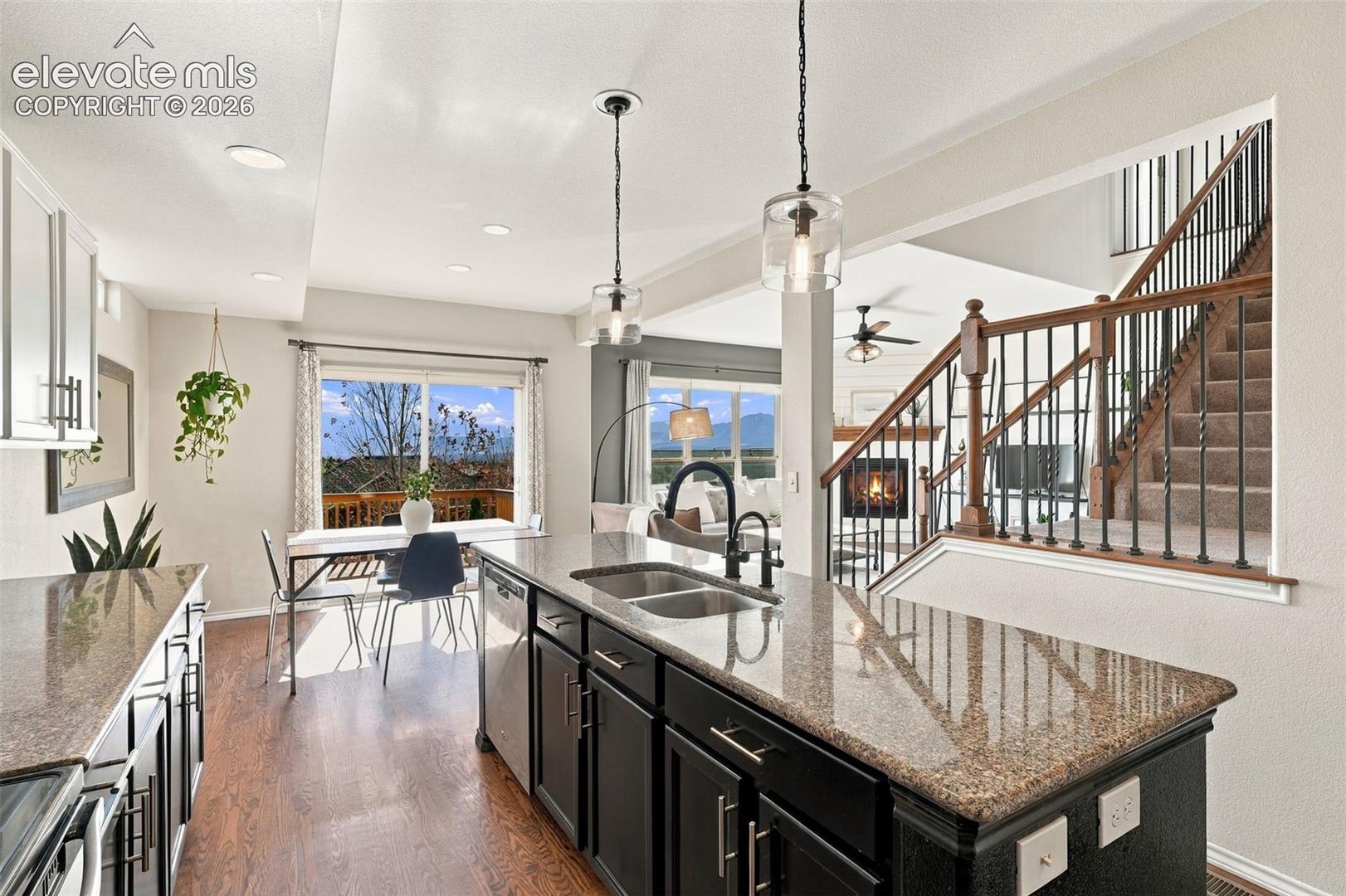 Kitchen featuring an island with stone-finish countertops, dark-tone cabinetry, wood-finish flooring, double-basin undermount sink with a high-arch faucet, and dual glass pendant lights