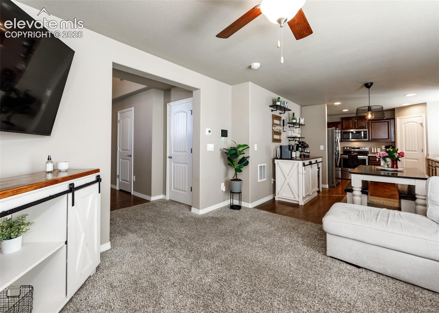 Built-in white cabinetry with sliding barn-style doors and stained-wood top, wall-mounted ceiling fan, recessed lighting, and kitchen cabinetry featuring a stone-surface island