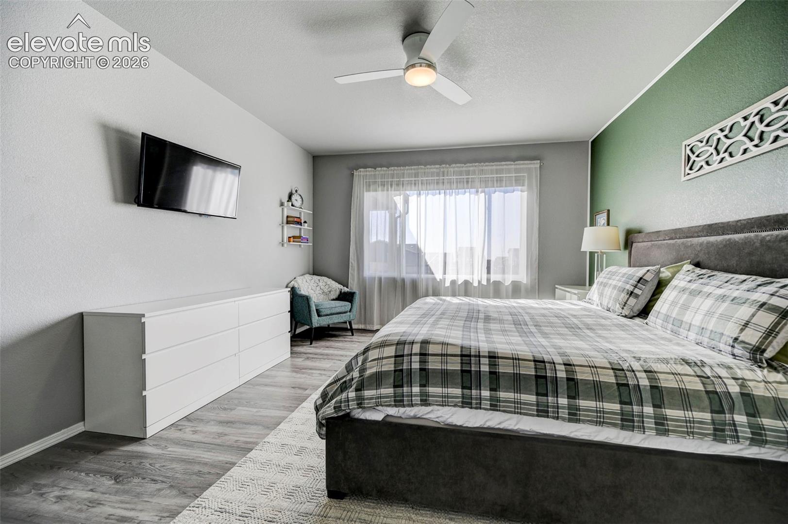 Bedroom featuring a textured accent wall, wood-finish flooring, and a ceiling fan with integrated lighting