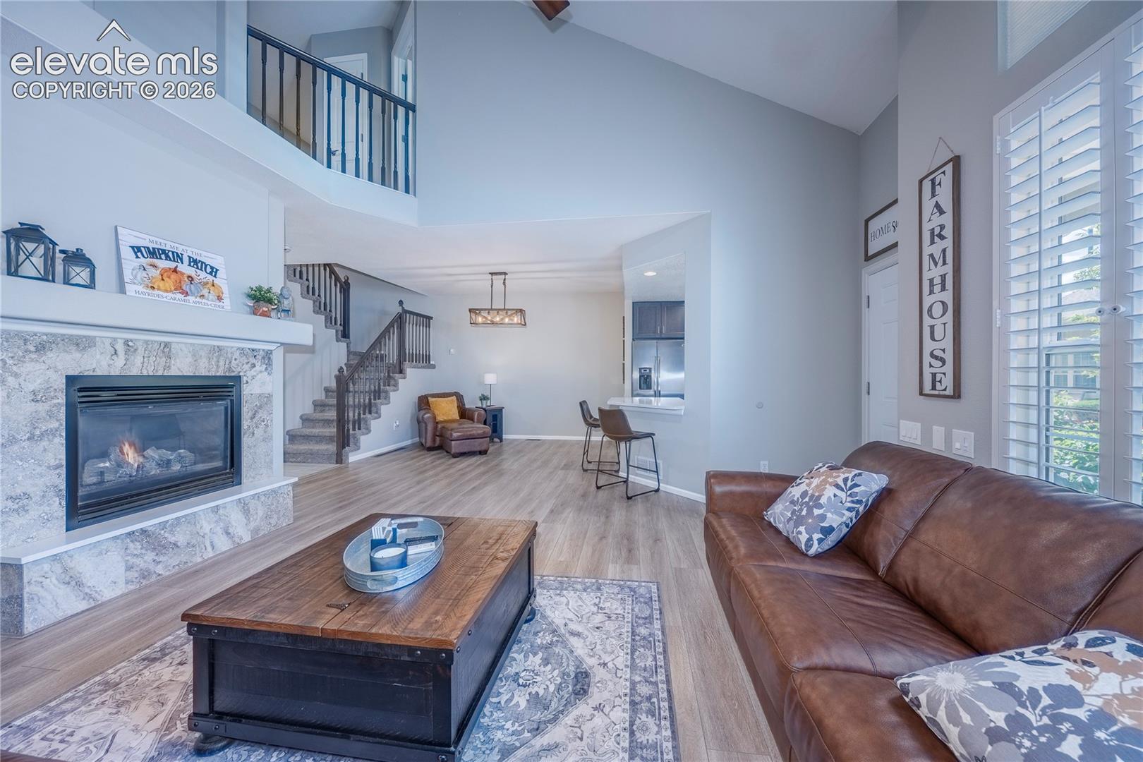 Vaulted ceilings featuring a floor-to-ceiling stone-surround fireplace, wood-finish flooring, plantation shutters, and a balcony overlook