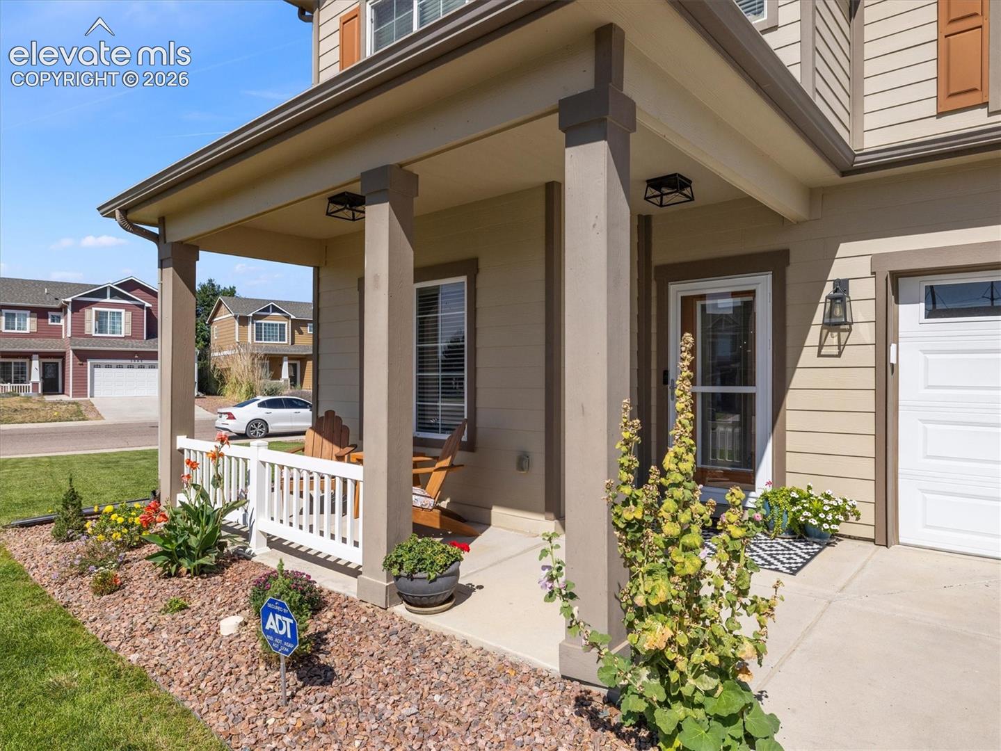 Covered front porch with white railing, stone accents, and manicured landscaping