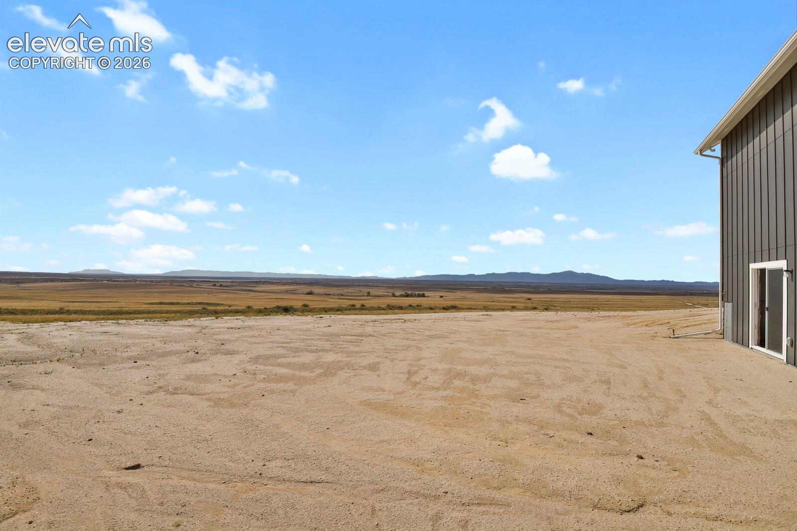 Expansive lot featuring vertical metal siding, glass sliding door, and mountain backdrop