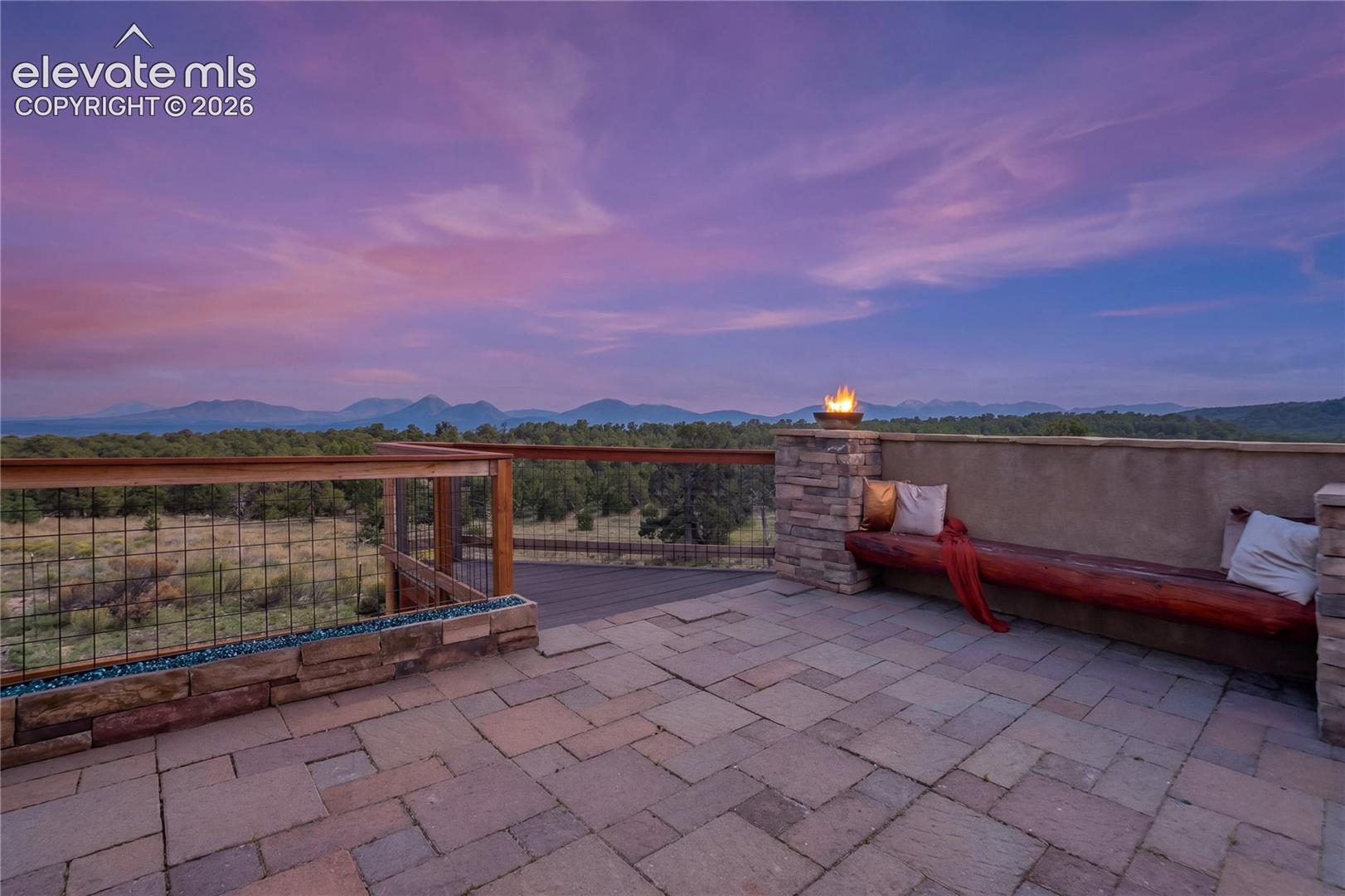 Paver patio with a stone-clad half-wall, built-in wooden bench, and a modern fire feature