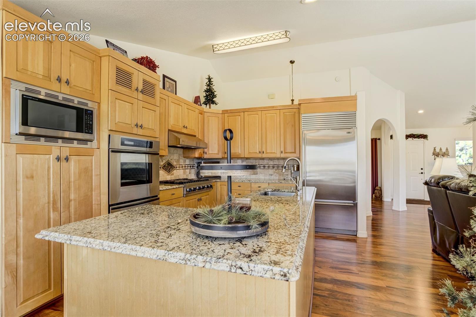 Kitchen featuring natural wood cabinetry, granite countertops, stainless steel appliances, an integrated island, and wood-finish flooring