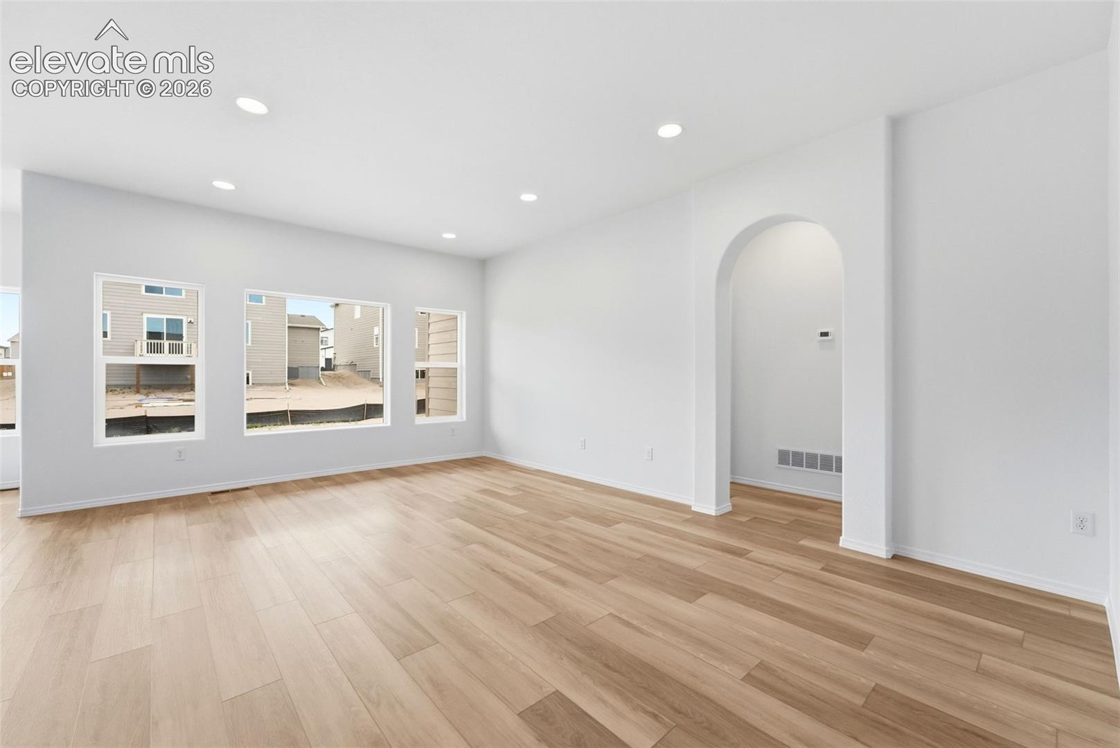 Living area featuring wood-finish flooring, recessed lighting, expansive windows, and an arched architectural opening