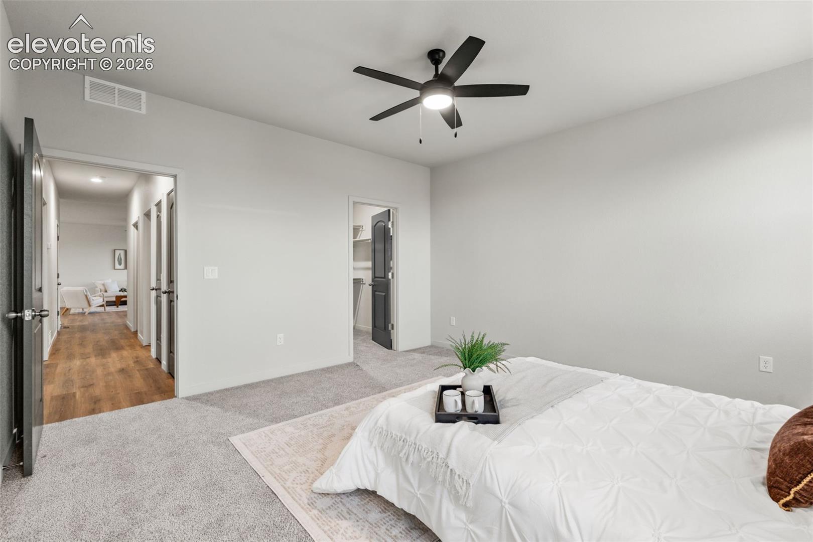 Neutral-toned bedroom featuring carpeted flooring, a ceiling fan with integrated lighting, and multiple paneled doors leading to a walk-in closet and hallway