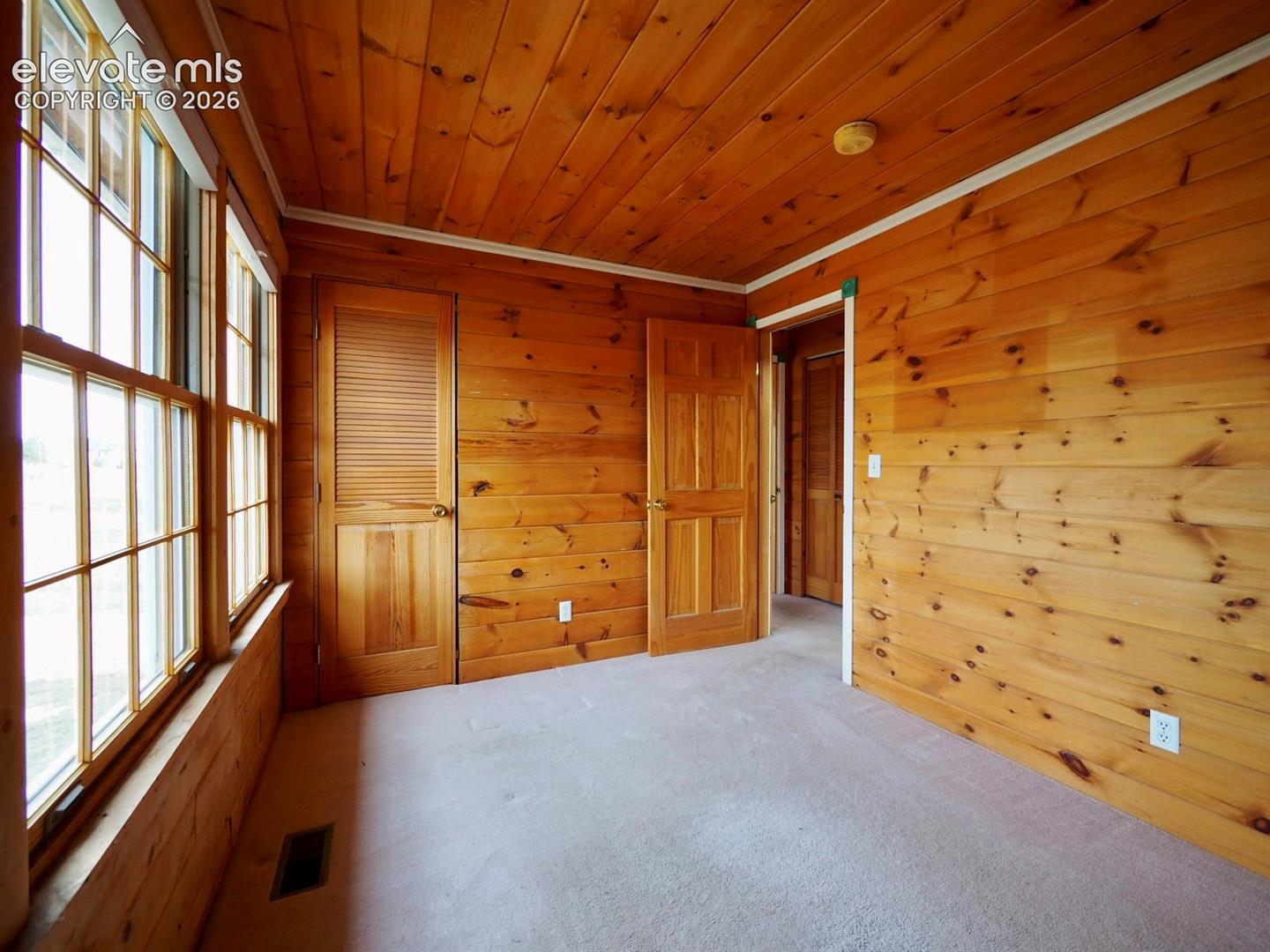 Natural wood-paneled walls and ceiling, multi-pane windows, louvered closet door, and interior paneled doors