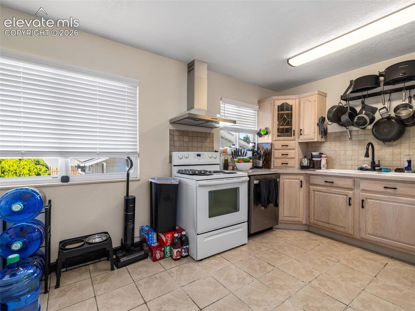 Kitchen featuring tile flooring, light wood-finish cabinetry, a stainless steel range hood, and a tile backsplash