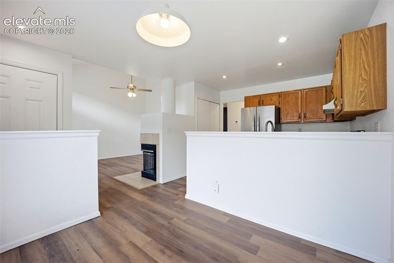 Wood-finish flooring, recessed lighting, fireplace with tile surround, built-in wooden cabinetry, and stainless steel kitchen appliances