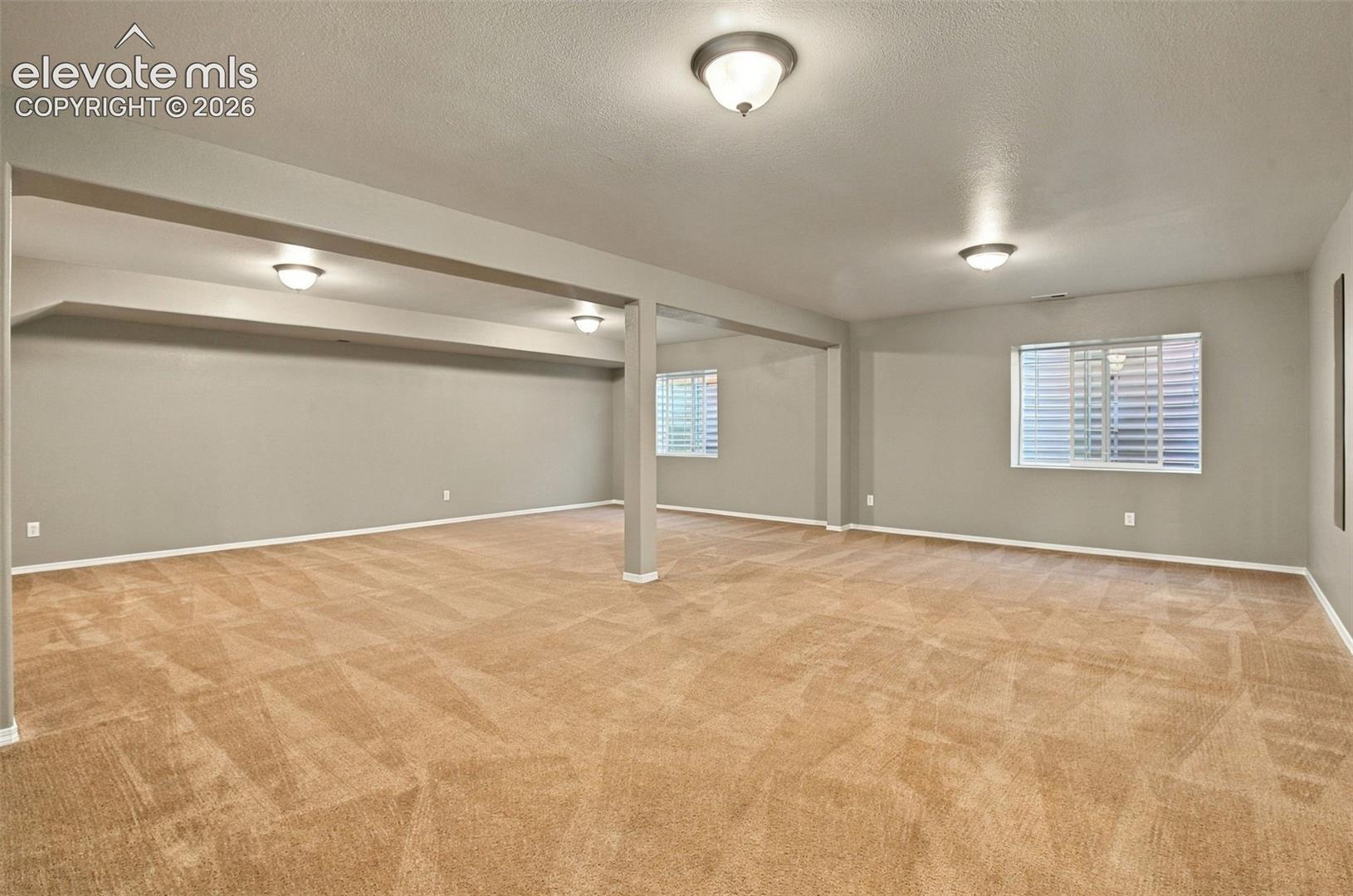 Expansive room featuring carpet flooring, multiple windows with blinds, and flush-mount ceiling fixtures