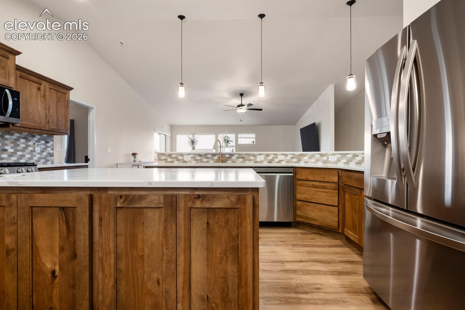 Kitchen featuring wood cabinetry, stone-finish countertops, stainless steel appliances, a multi-tonal hexagonal tile backsplash, and overhead pendant lighting