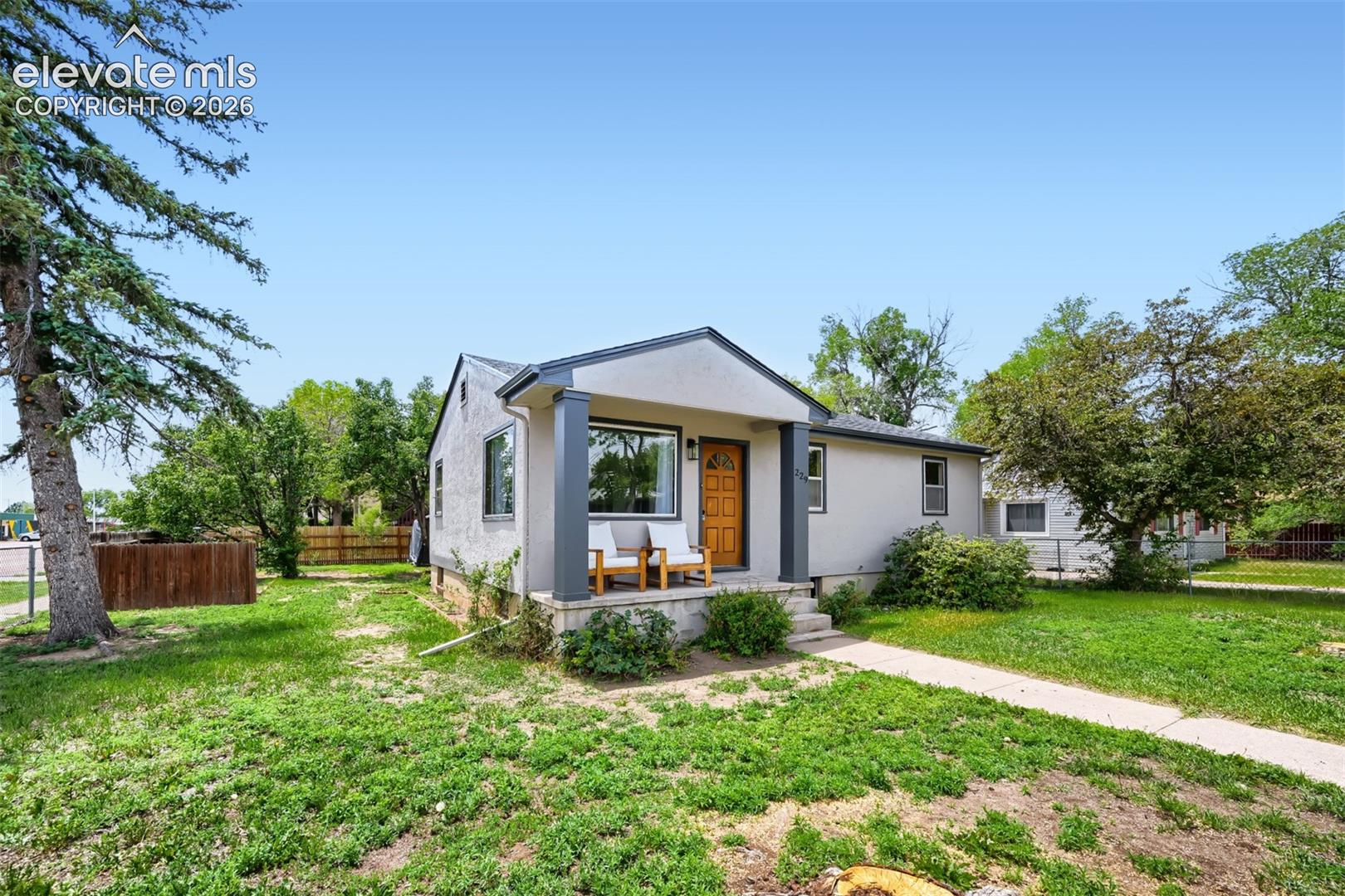 Stucco exterior with a covered front porch, wood-finish front door, and established landscaping