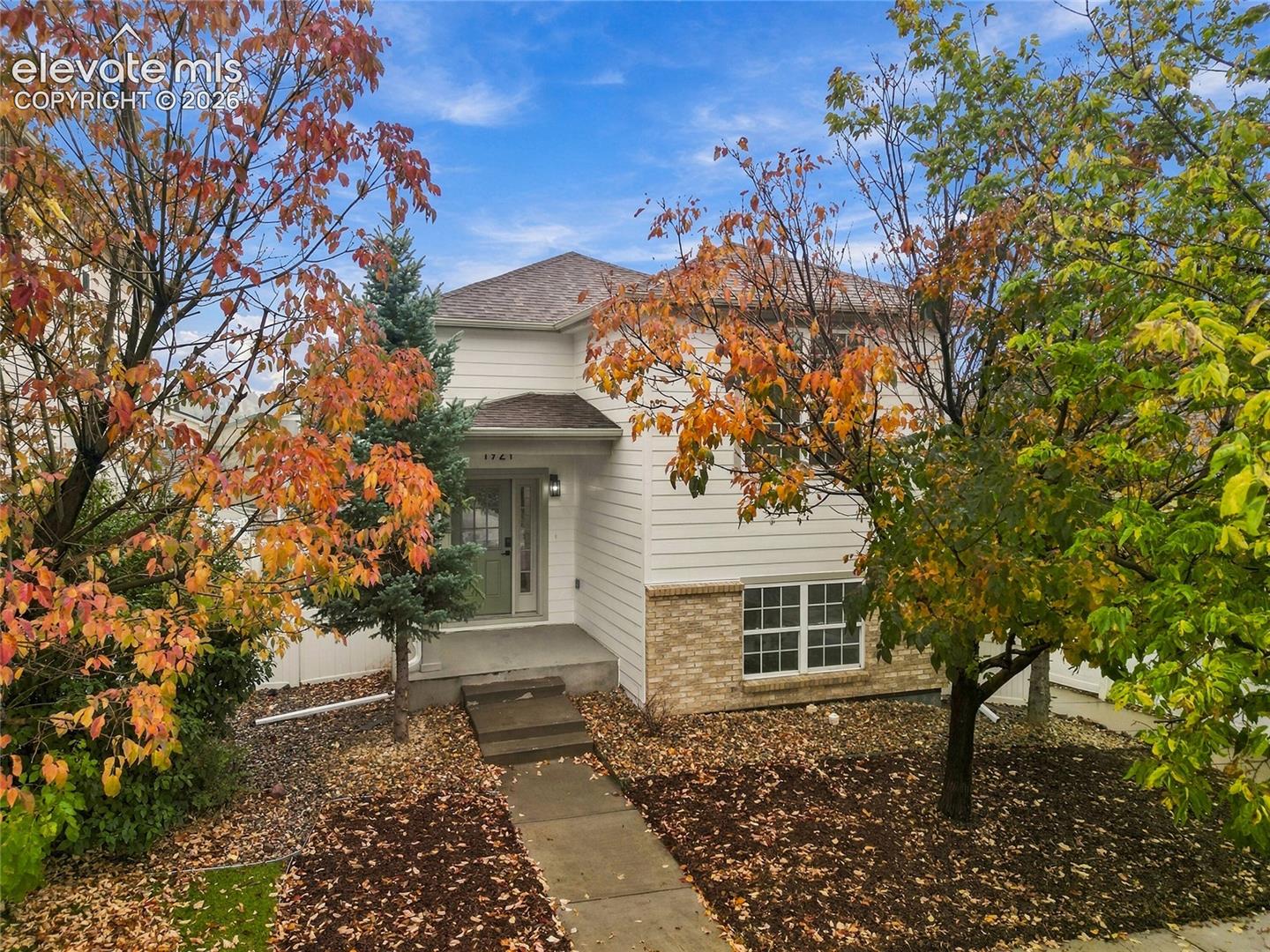 Two-story exterior featuring light-toned horizontal siding, a stone-veneer foundation accent, a covered entryway with a concrete porch, and multi-pane windows