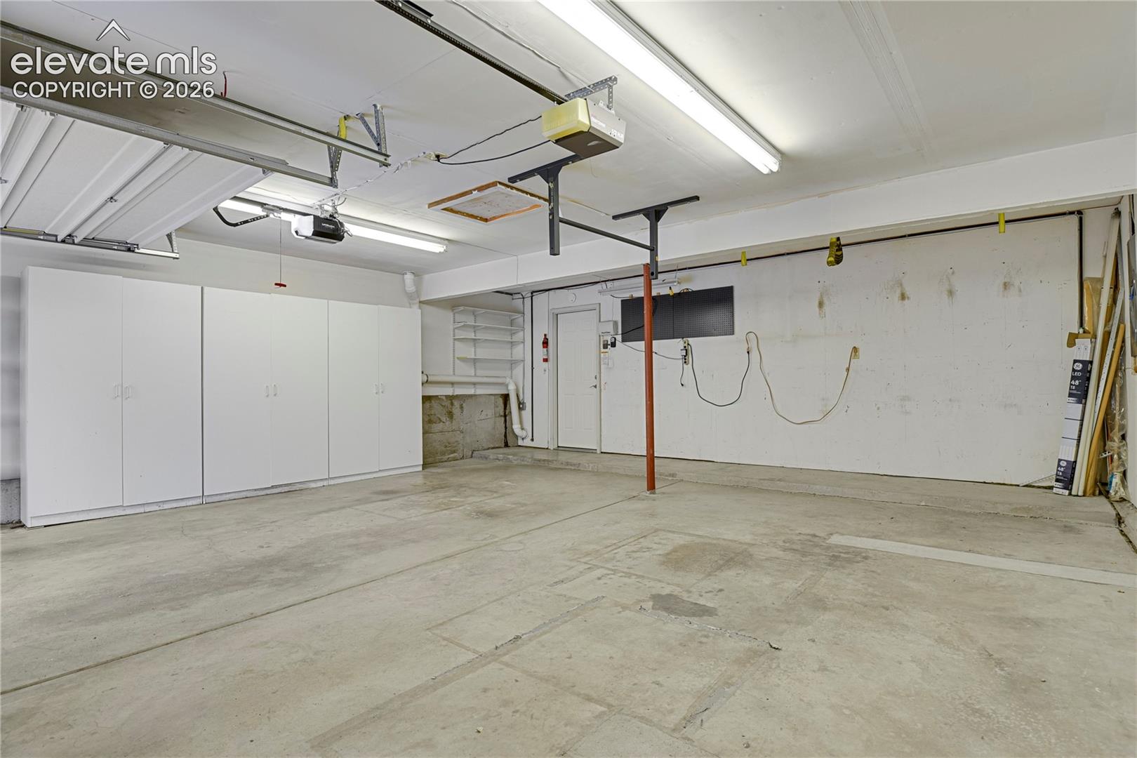 Attached garage featuring concrete flooring, built-in white cabinetry, integrated overhead lighting, and dedicated storage shelving