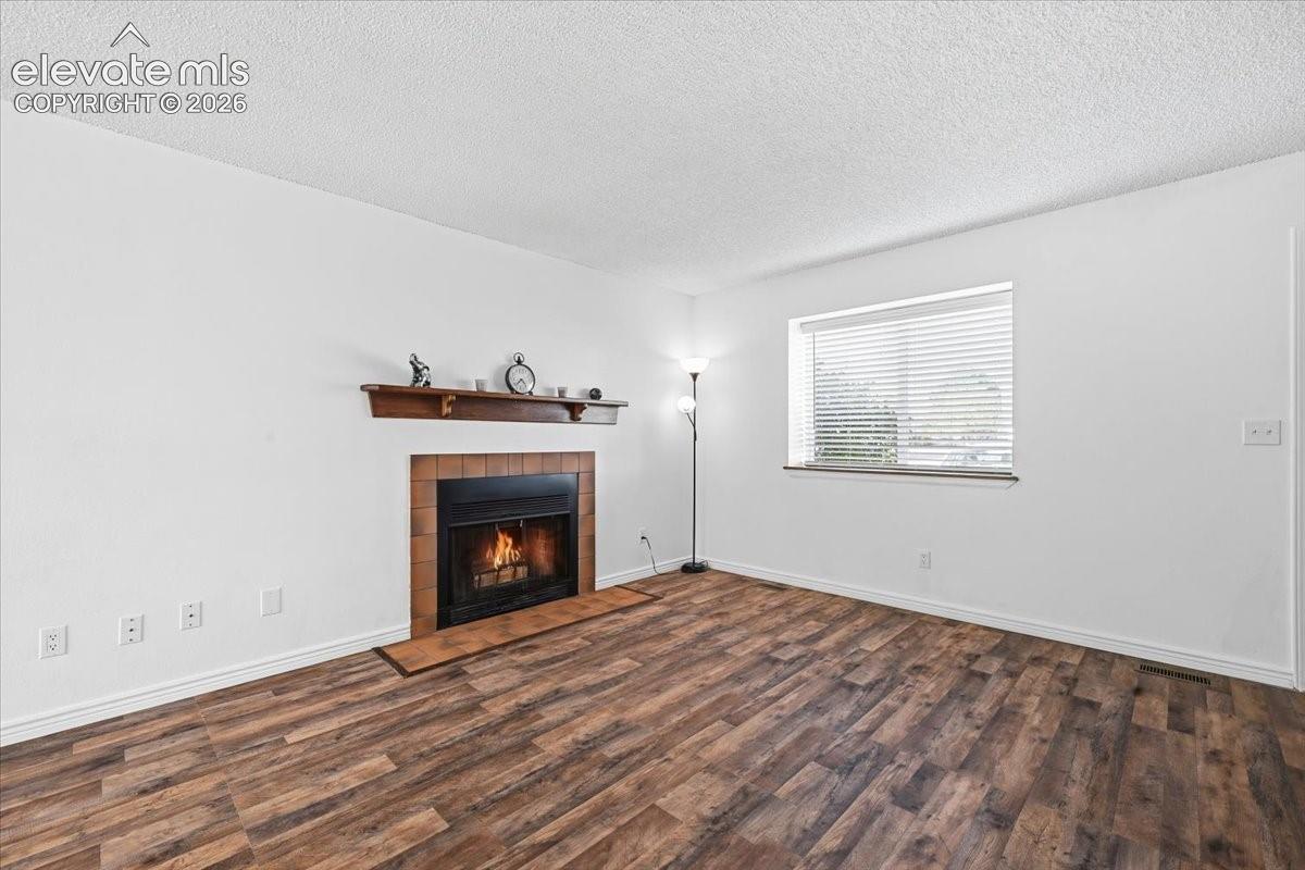 Wood-finish flooring, brick-surround fireplace with a wood mantel, and window with horizontal blinds