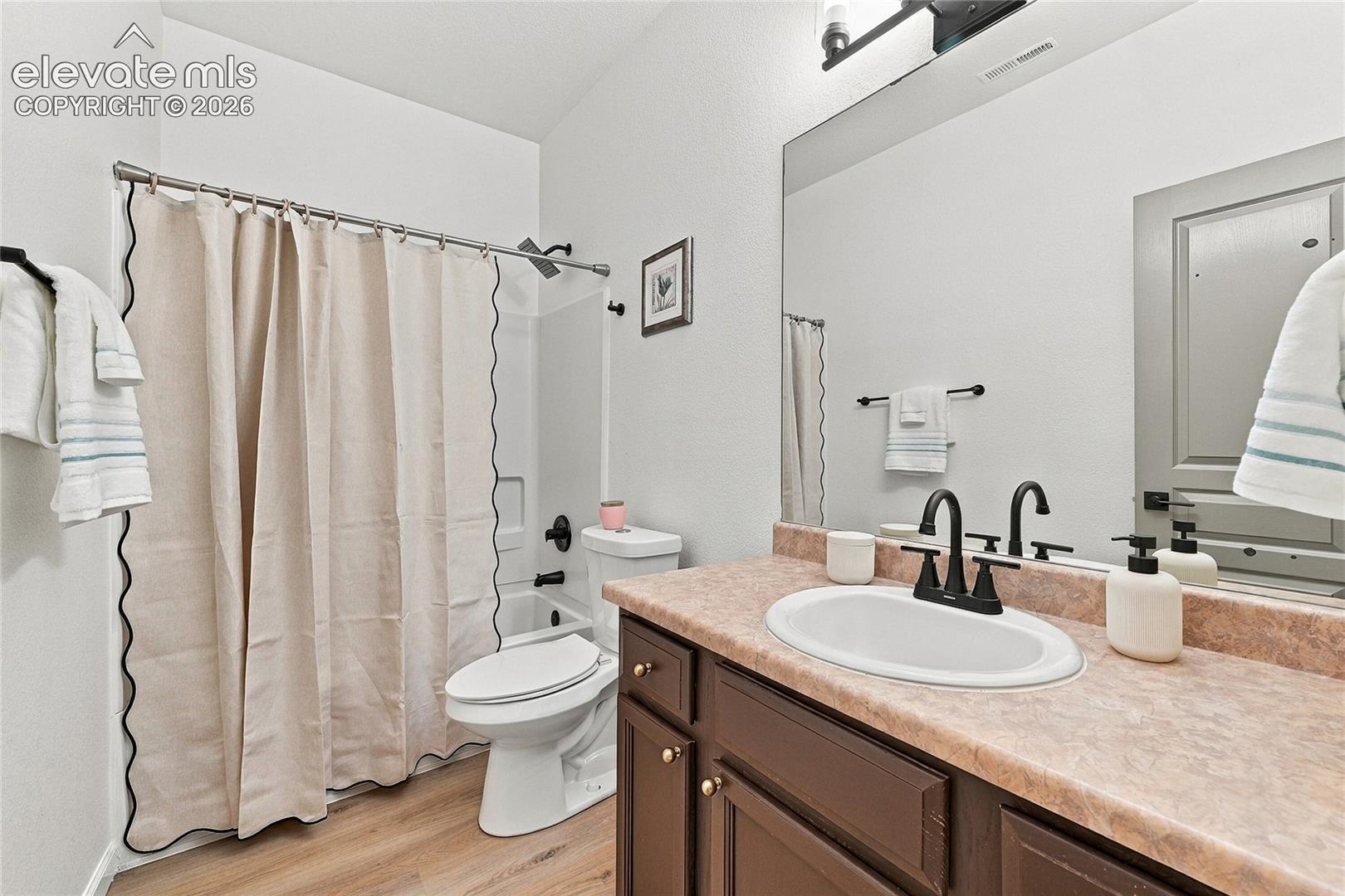 Full bathroom featuring wood-finish flooring, a vanity with a stone-composite countertop, an undermount sink with matte black hardware, and a tub-shower combination