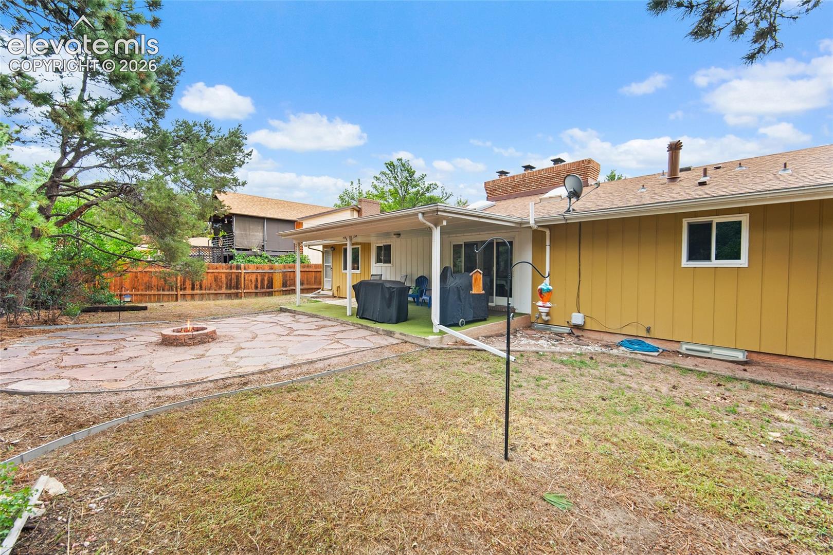 Backyard featuring a covered patio, flagstone fire pit area, wood-style privacy fencing, and masonry chimney