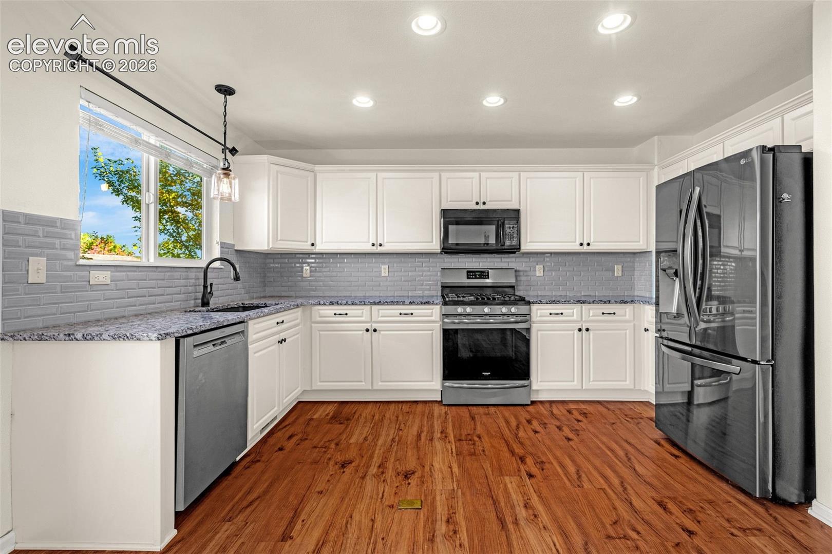 Kitchen featuring white cabinetry, stone-surface countertops, subway tile backsplash, stainless steel appliances, and wood-finish flooring
