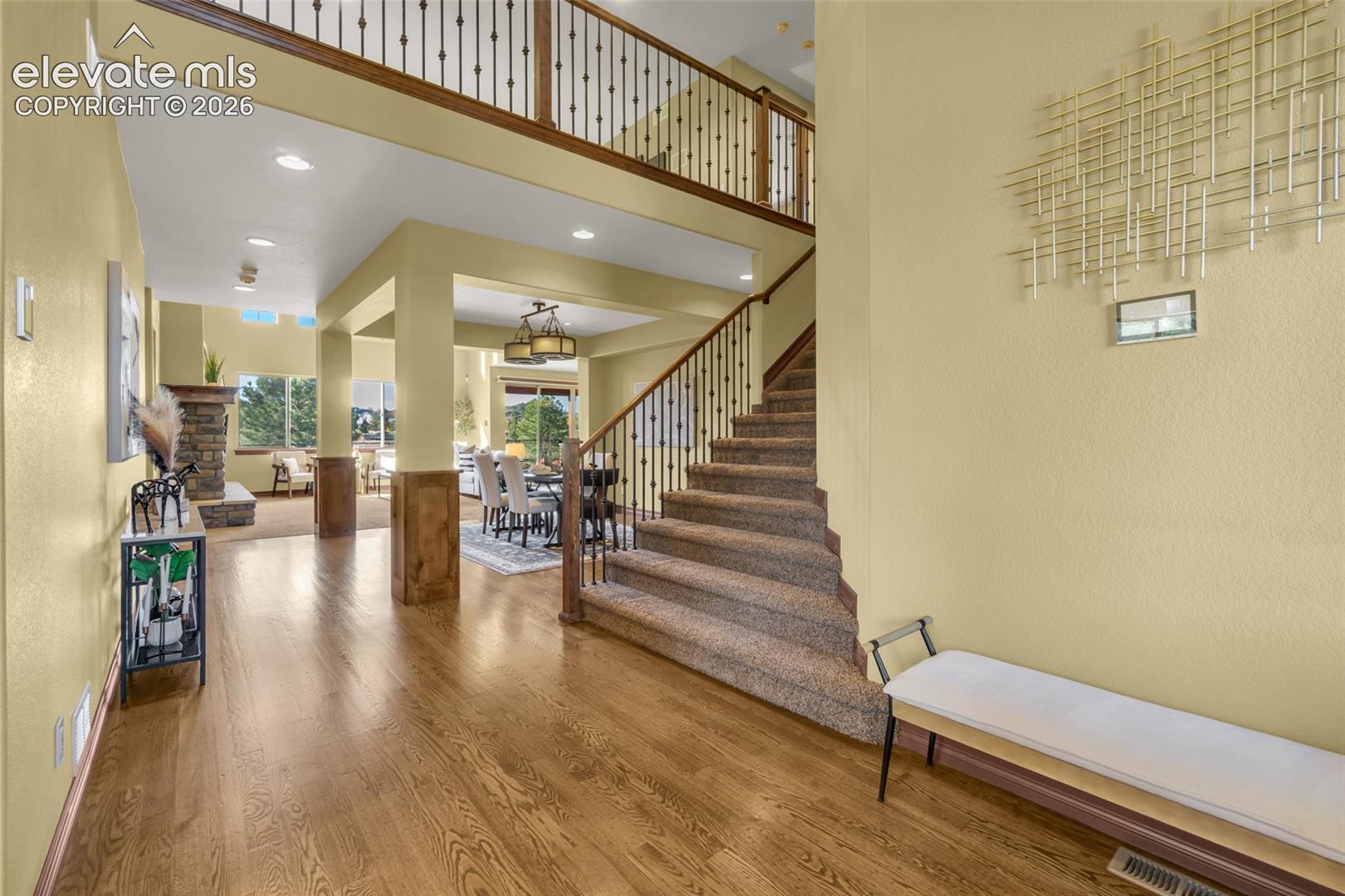 Foyer featuring wood-finish flooring, a two-story ceiling, a staircase with metal balusters and wood handrails, recessed lighting, and a stone-accented hearth