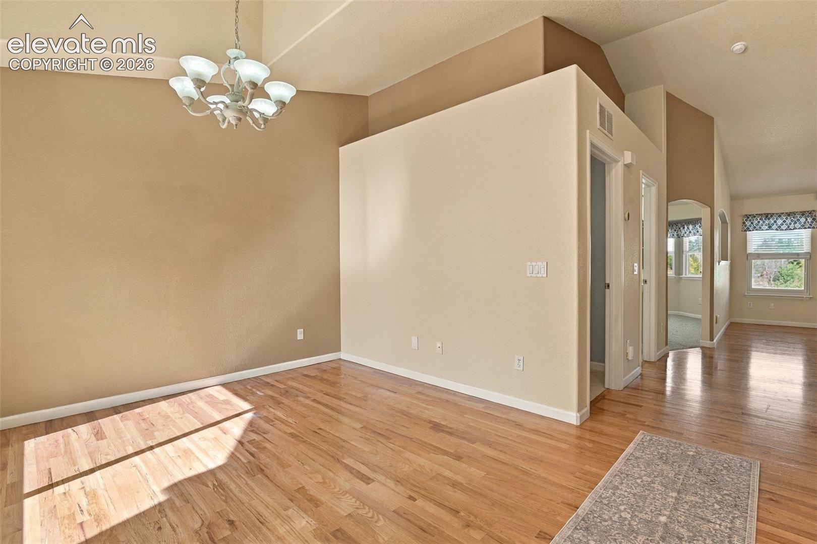 Vaulted ceilings, wood-finish flooring, and a multi-arm chandelier featuring frosted glass shades
