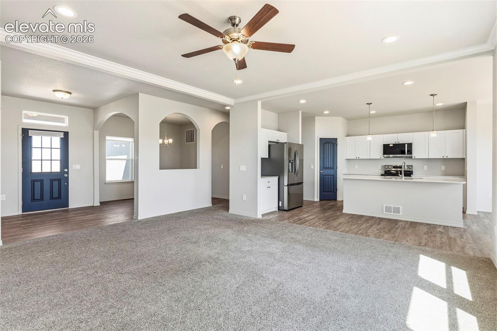 Expansive open concept living area featuring a ceiling fan with light fixture, recessed lighting, and crown molding
