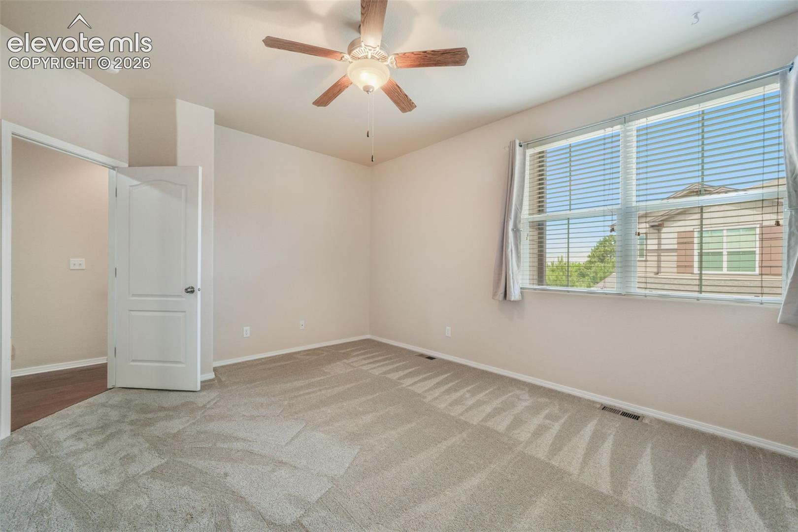 Carpeted room with a ceiling fan light fixture, a wide window with blinds, and a white paneled door