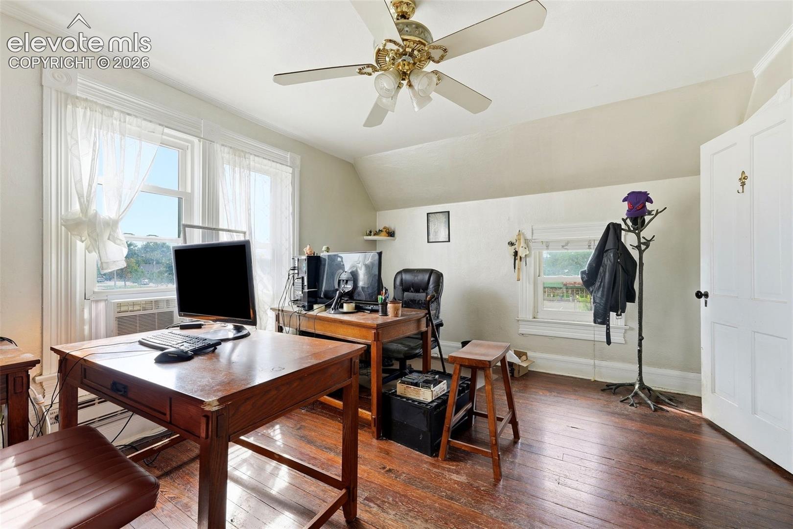 Hardwood flooring, multiple windows, ceiling fan, white paneled door, sloped ceiling