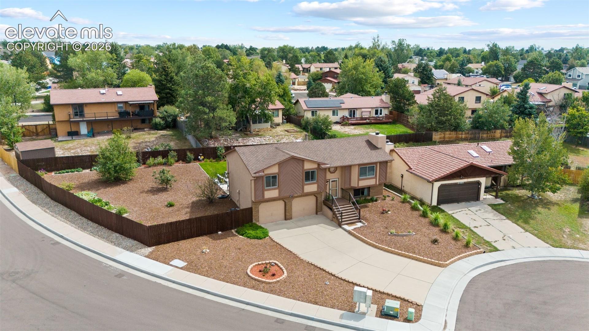 Split-level residence featuring a two-car attached garage, concrete driveway, wood-paneled exterior siding, composite shingle roof, and a fenced corner lot