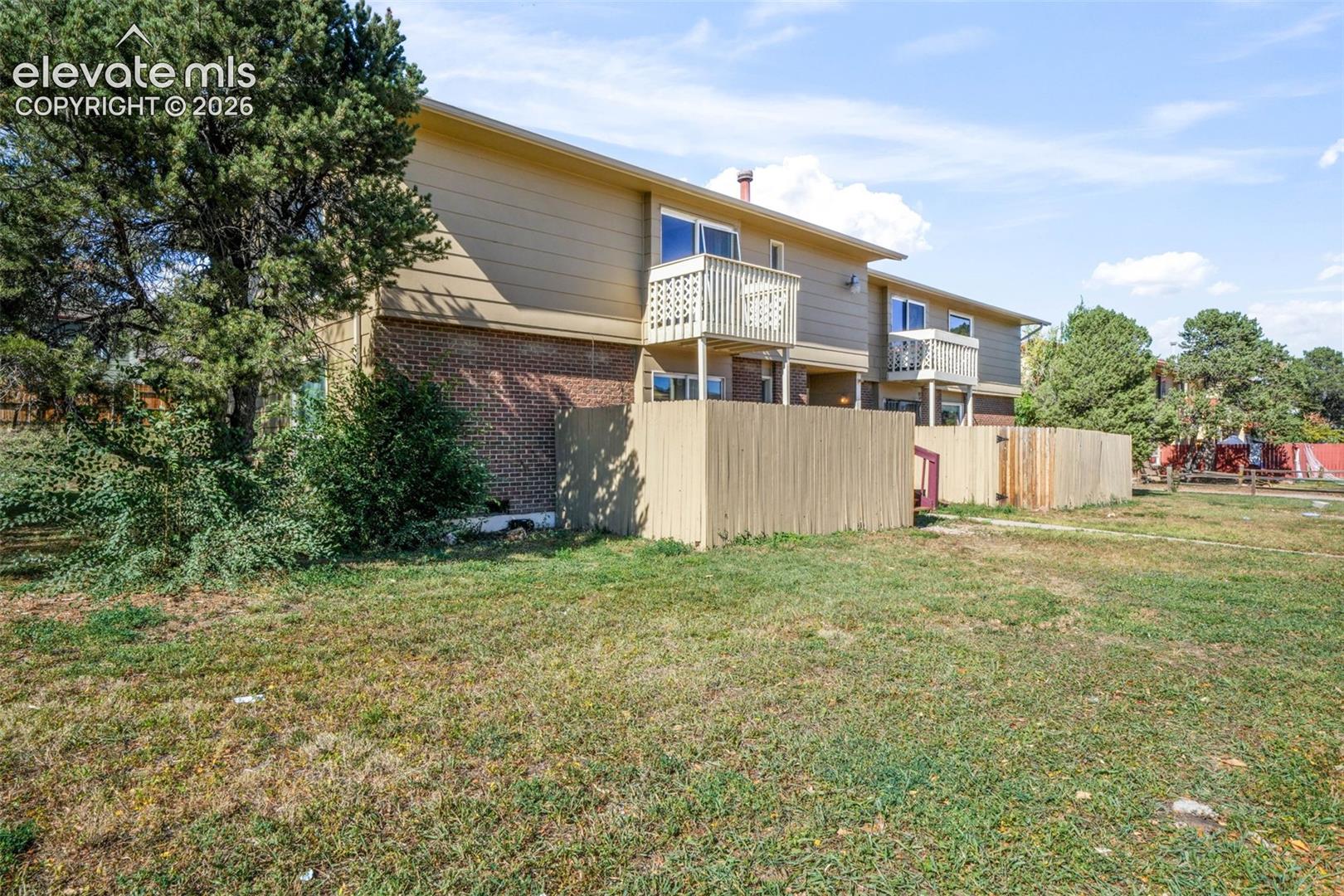 Two-story building exterior featuring a brick and horizontal siding facade, private balconies, and enclosed fenced yard areas