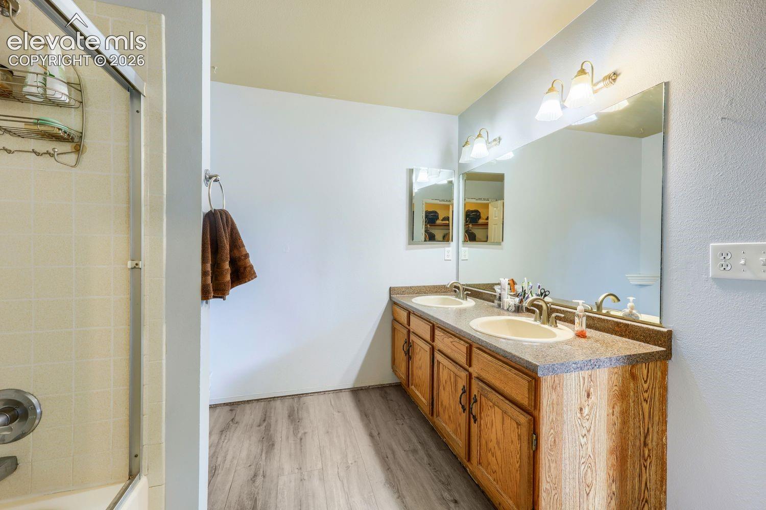 Dual vanity with wood-finish cabinetry, integrated sinks, and a large wall-mounted mirror