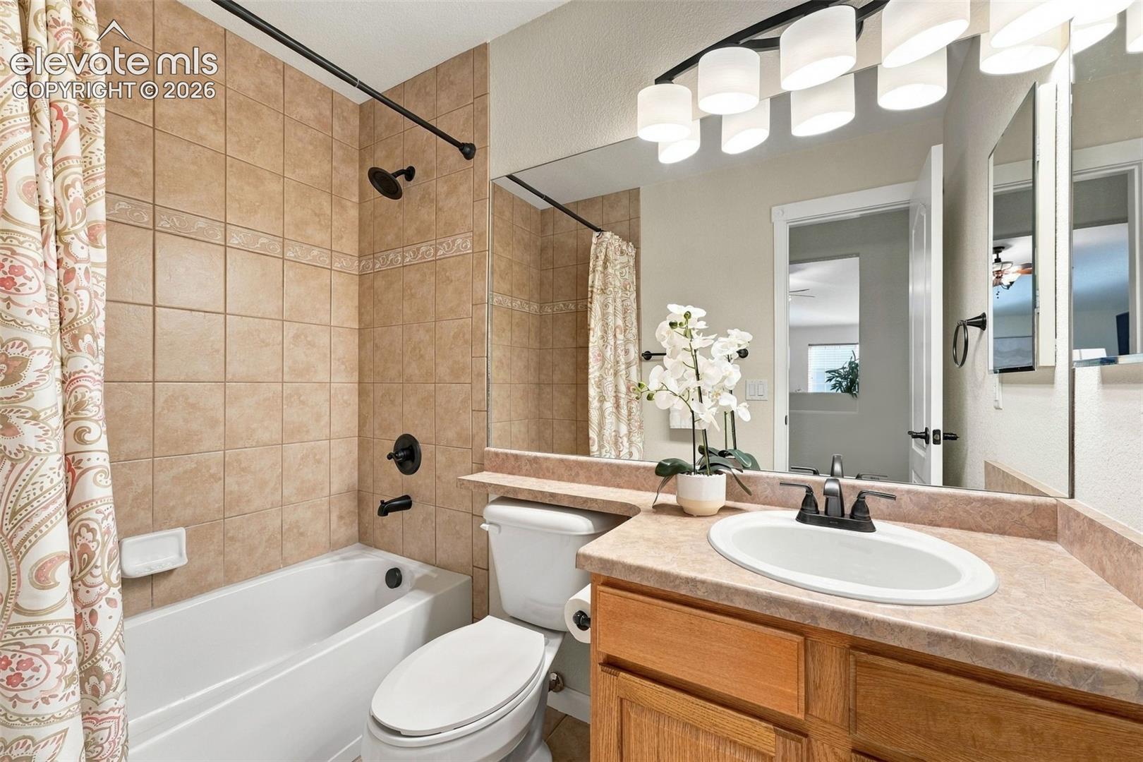 Bathroom featuring a built-in bathtub with a tile surround, vanity with an undermount sink and dark hardware, large wall-mounted mirror, and multi-bulb overhead lighting fixture
