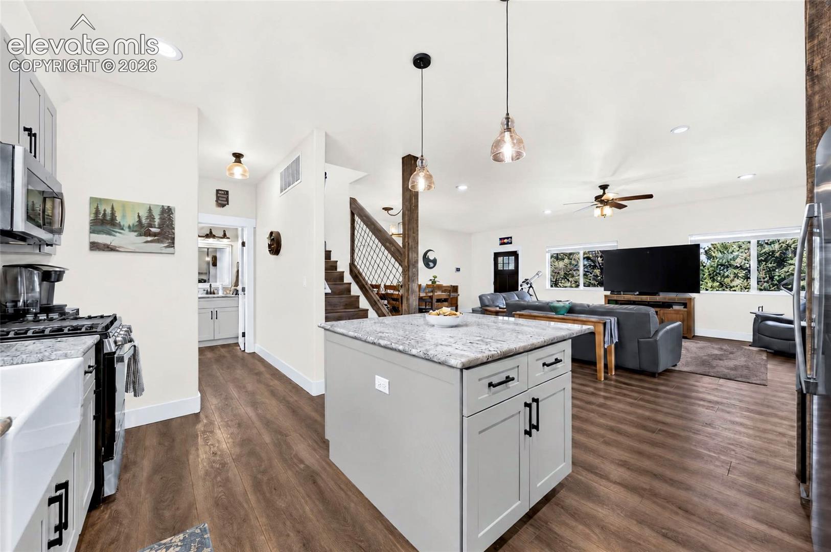 Kitchen featuring a central island with a stone-finish countertop, wood-finish flooring, apron-front sink, and pendant lighting