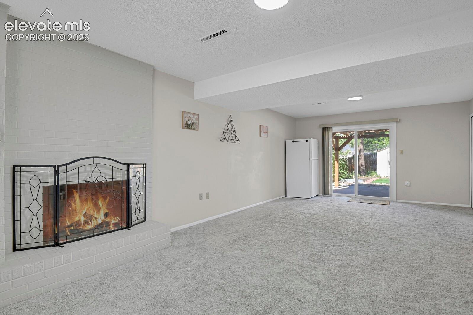 Spacious recreation room featuring neutral carpeting, recessed ceiling lighting, and a decorative fireplace screen