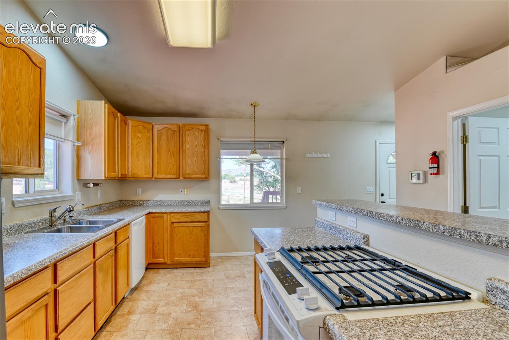 Kitchen featuring wood cabinetry, speckled laminate countertops, a dual-basin stainless steel sink, and a built-in gas range cooktop