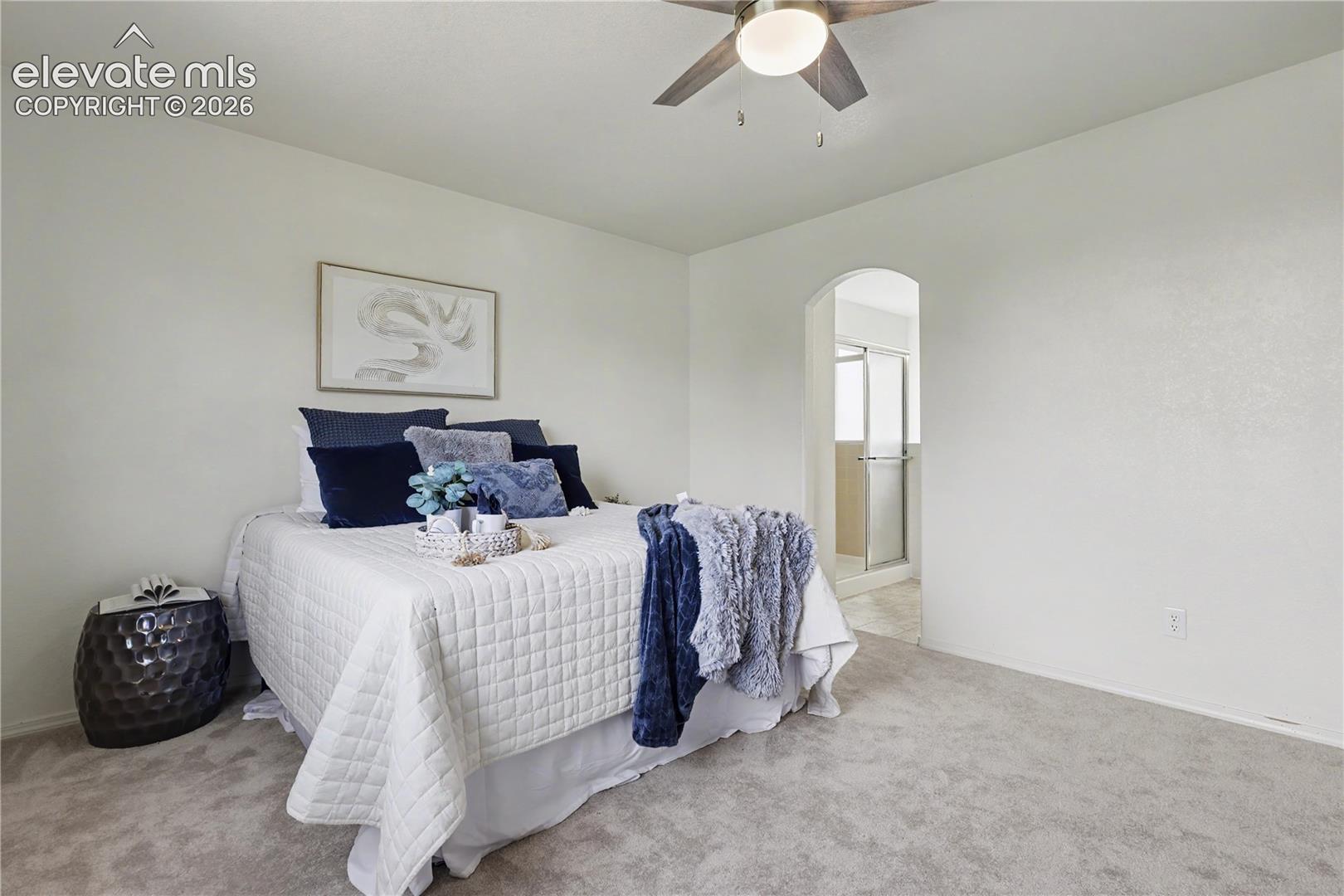 Carpeted room featuring a ceiling fan, arched doorway, and an en-suite bath with a glass-enclosed shower