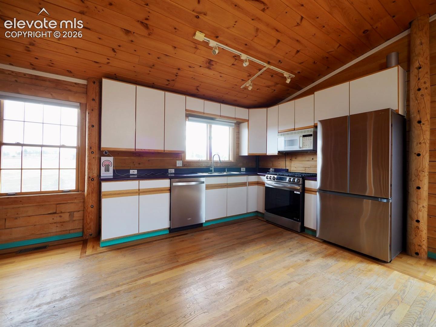 Kitchen featuring wood-paneled walls and ceilings, white cabinetry, dark countertops, wood flooring, and stainless steel appliances