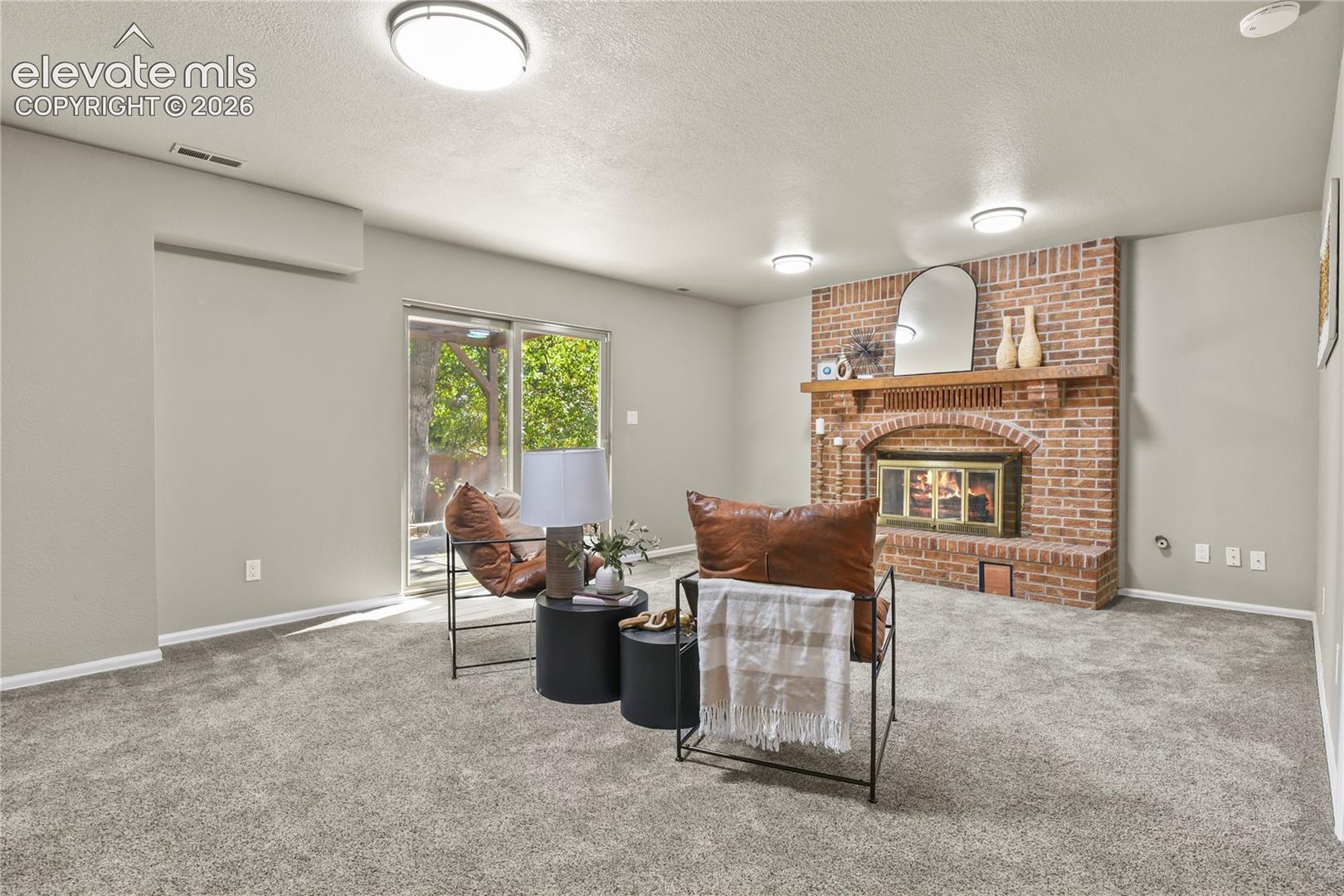 Living area featuring a brick fireplace with an arched hearth, a wooden mantel, neutral carpeting, and a sliding glass door
