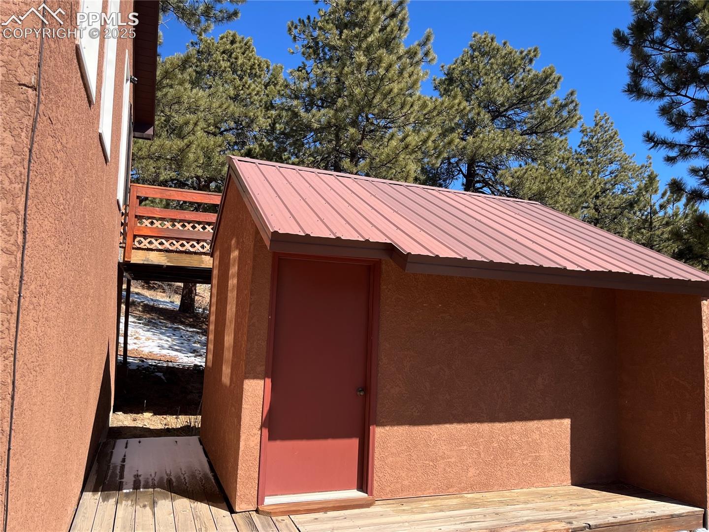 East side of the building with deck.  A large storage area.   Home has a metal roof.