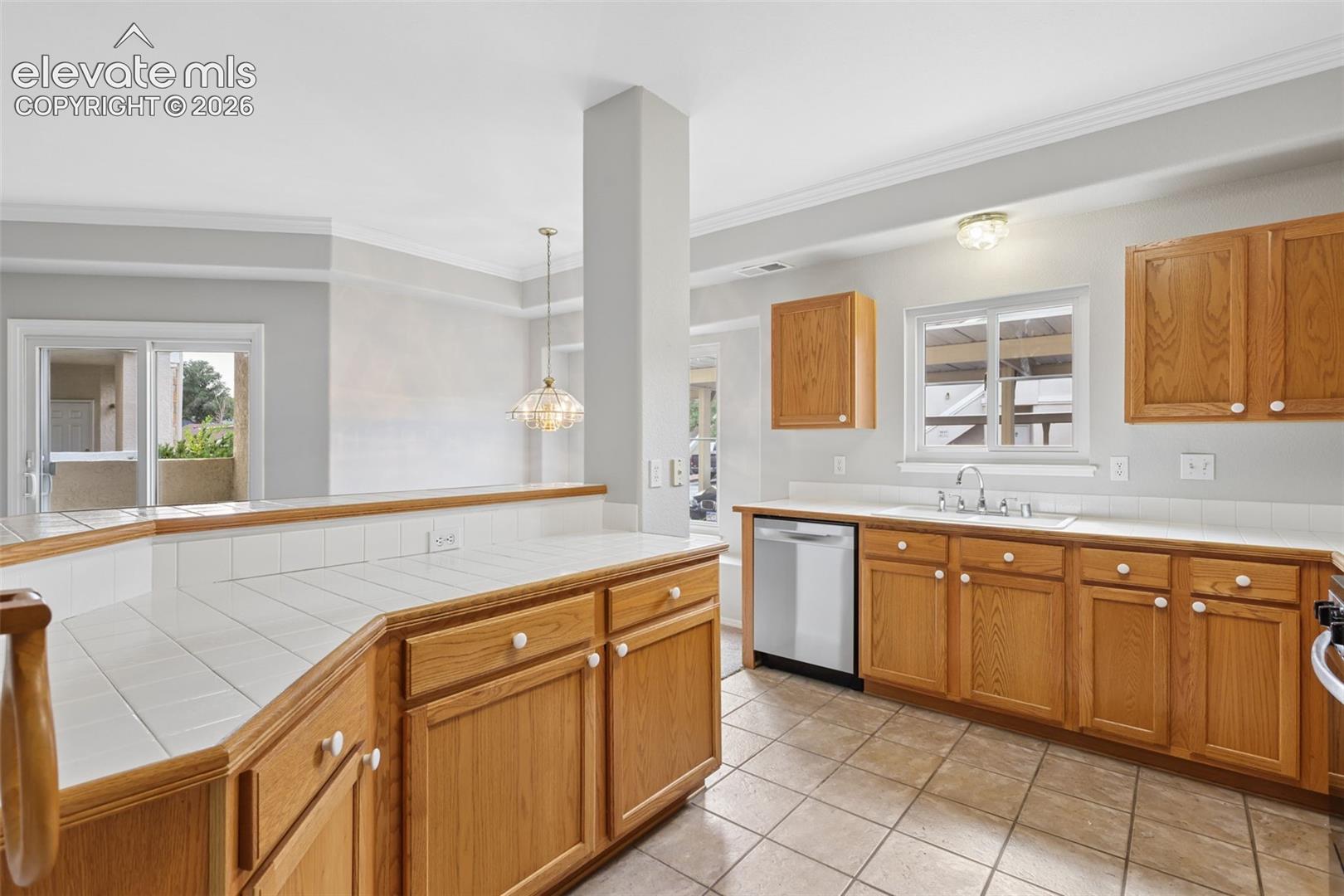 Kitchen with wood-finish cabinetry, tile countertops, and a stainless steel dishwasher