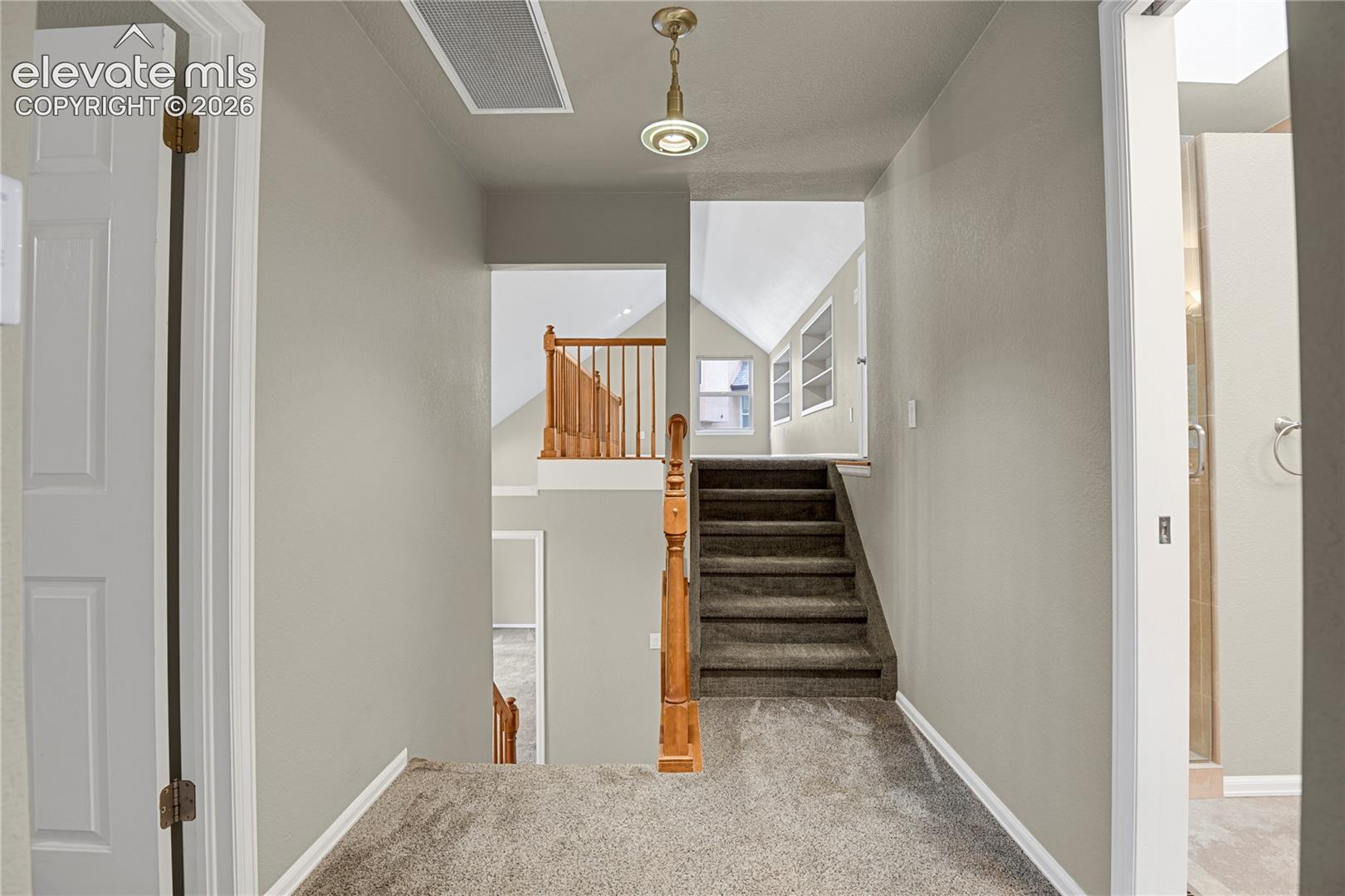 Hallway featuring neutral wall paint, carpeted flooring, a metallic pendant light fixture, and wooden staircase railing