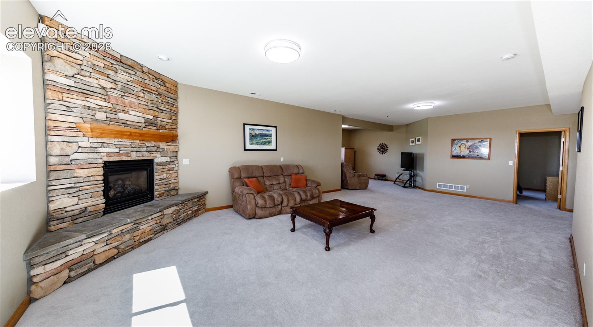 Stone-clad fireplace with a wood mantle, an integrated hearth, and a carpeted floor