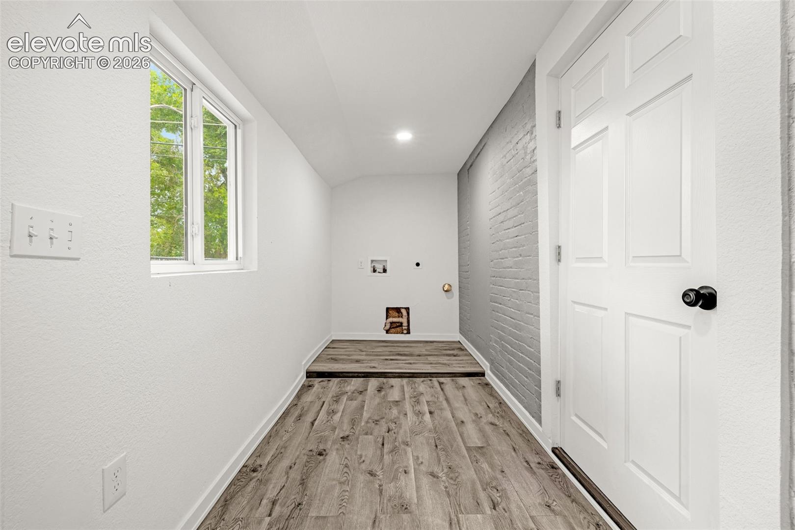 Utility room featuring a painted brick accent wall, wood-finish flooring, a contemporary window, and a paneled door with a black knob