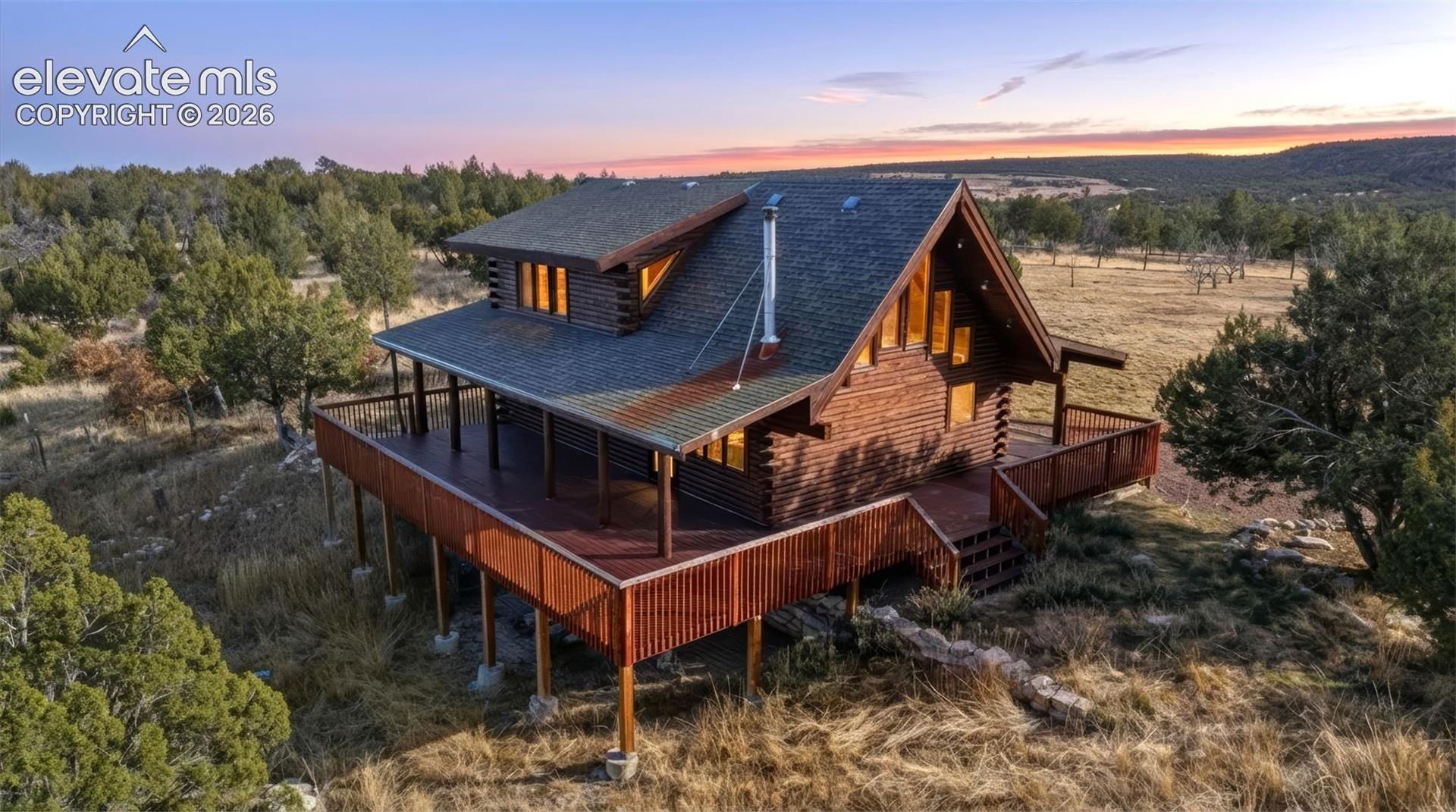 Log home exterior featuring a pitched roof, full-length deck, and a prominent chimney