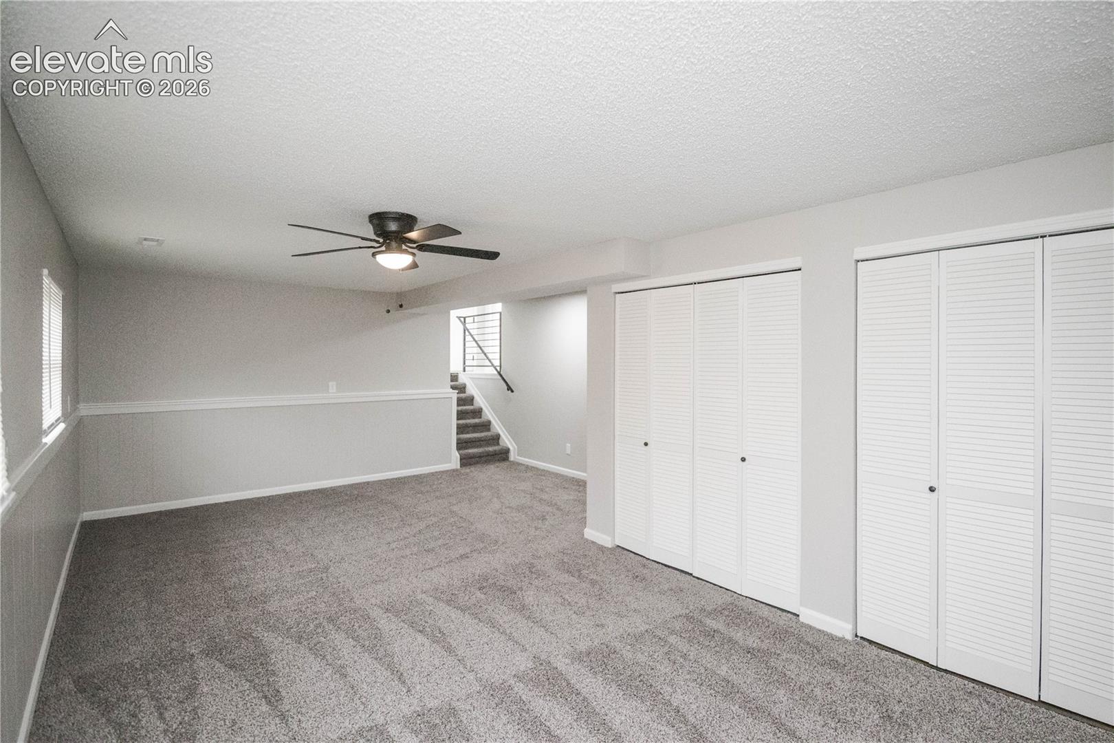Interior space featuring wall-to-wall carpeting, dual floor-to-ceiling closets with louvered doors, chair rail molding, and a ceiling-mounted light fixture with a fan