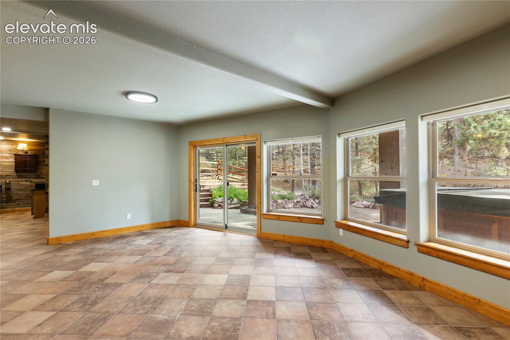 Interior space featuring large-format tile flooring, natural wood trim, sliding glass door, and oversized windows