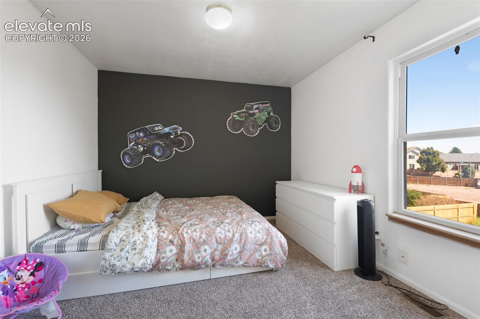 Carpeted room featuring a white paneled bed frame, a dark accent wall, and a large window with white framing