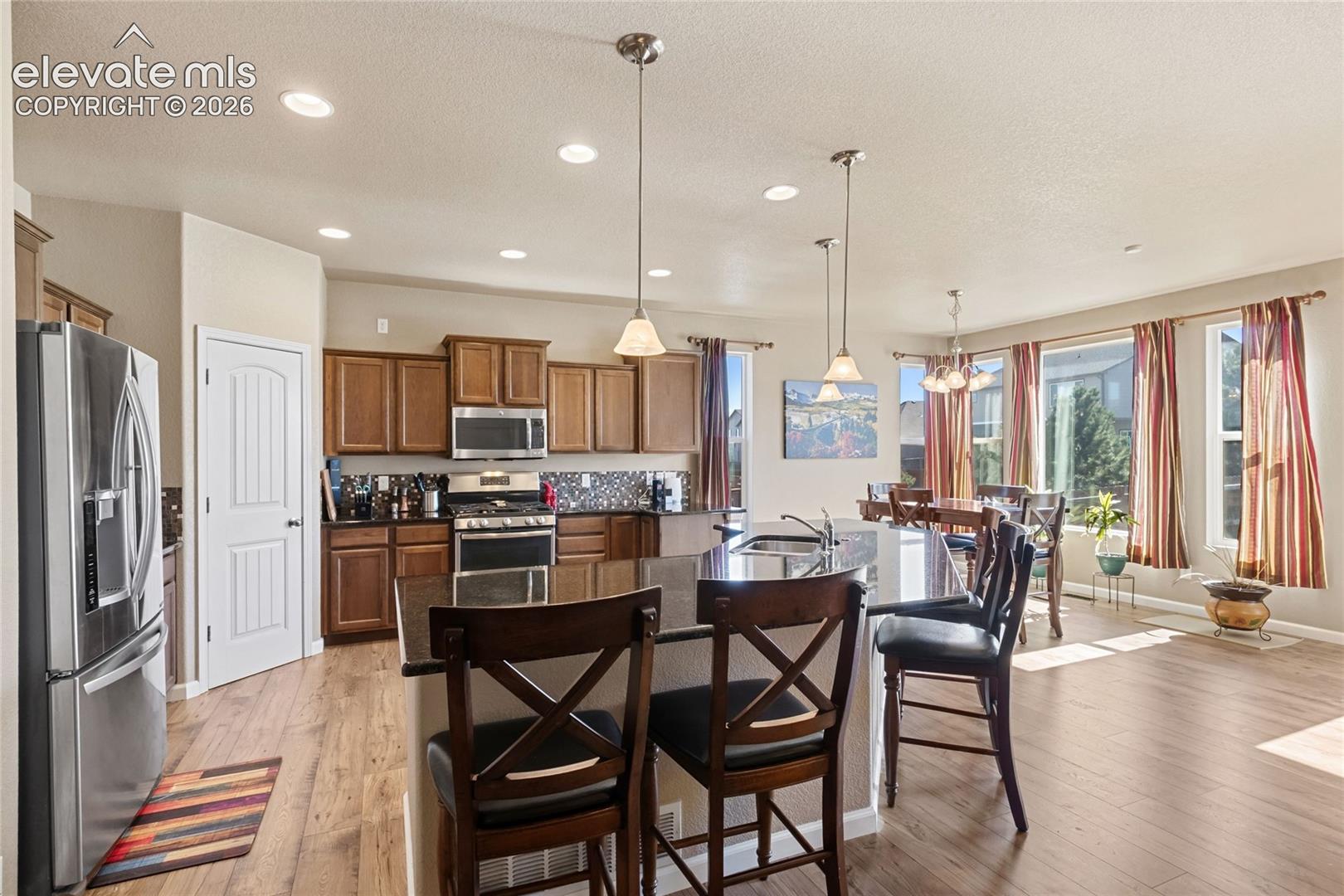 Kitchen featuring wood-finish cabinetry, stone-surface center island, recessed lighting, stainless steel appliance package, and wood-finish flooring