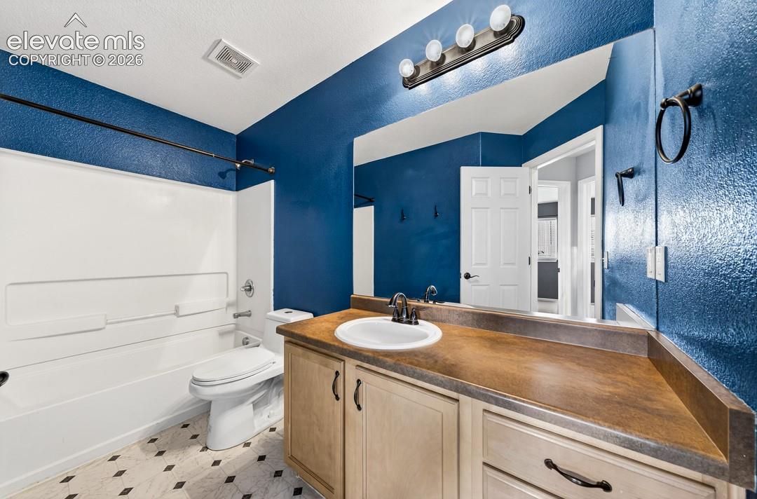 Bathroom featuring a vanity with wood-tone cabinetry, a solid-surface countertop, an oval undermount sink, and a large wall-mounted mirror