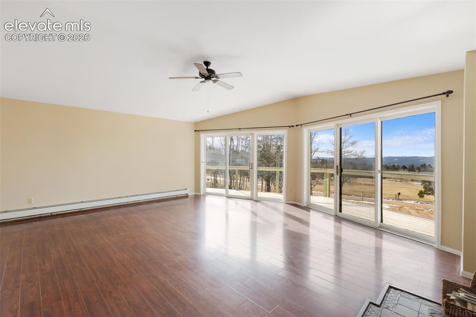 Wood-finish flooring, vaulted ceiling, ceiling fan, multiple sliding glass doors, and expansive outdoor scenery